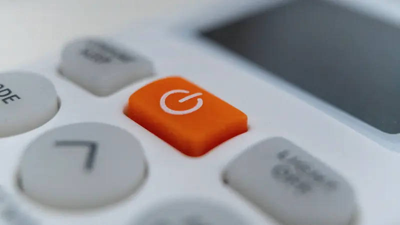 Gros plan sur les touches d'une télécommande, dont un bouton orange de mise en marche