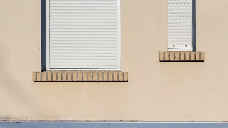 Façade claire avec une fenêtre dont le volet roulant blanc est fermé